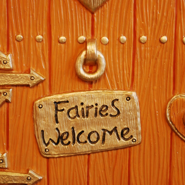 Decorative fairy door with 'Fairies Welcome' sign on a natural background