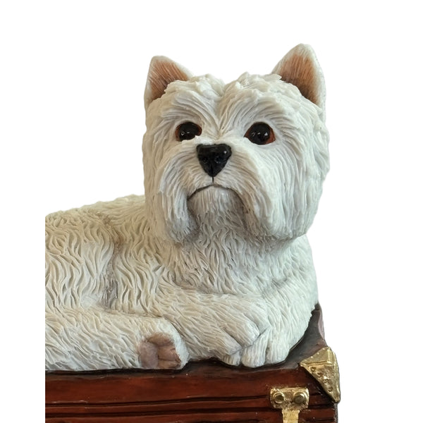 A white West Highland terrier dog figurine sitting on top of a brown vintage suitcase with gold-tone hardware