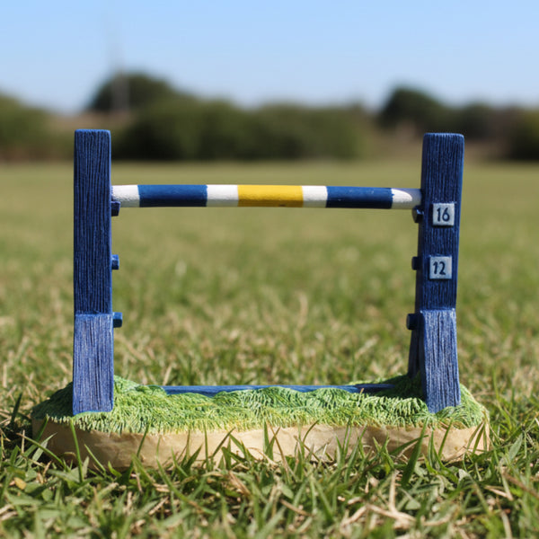 A dog agility trophy featuring a blue and yellow striped jump bar on top of a wooden base, designed to resemble grass.